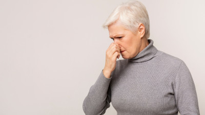 Ältere Dame fasst sich an die Nase. Schlechter Geruchsinn kann ein Hinweis auf eine koronare Herzkrankheit (KHK) sein