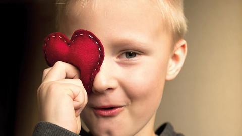 Kind hält sich ein Stoffherz ans Auge
