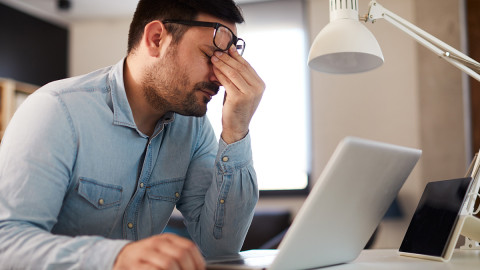 Mann fasst sich mit der Hand an den Kopf und sitzt vor dem Laptop