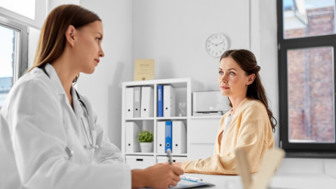 Ärztin und junge Patientin unterhalten sich in der Praxis am Schreibtisch.