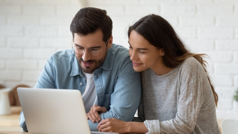 Ein junges Paar sitzt am Küchentisch und schaut auf ein Laptop